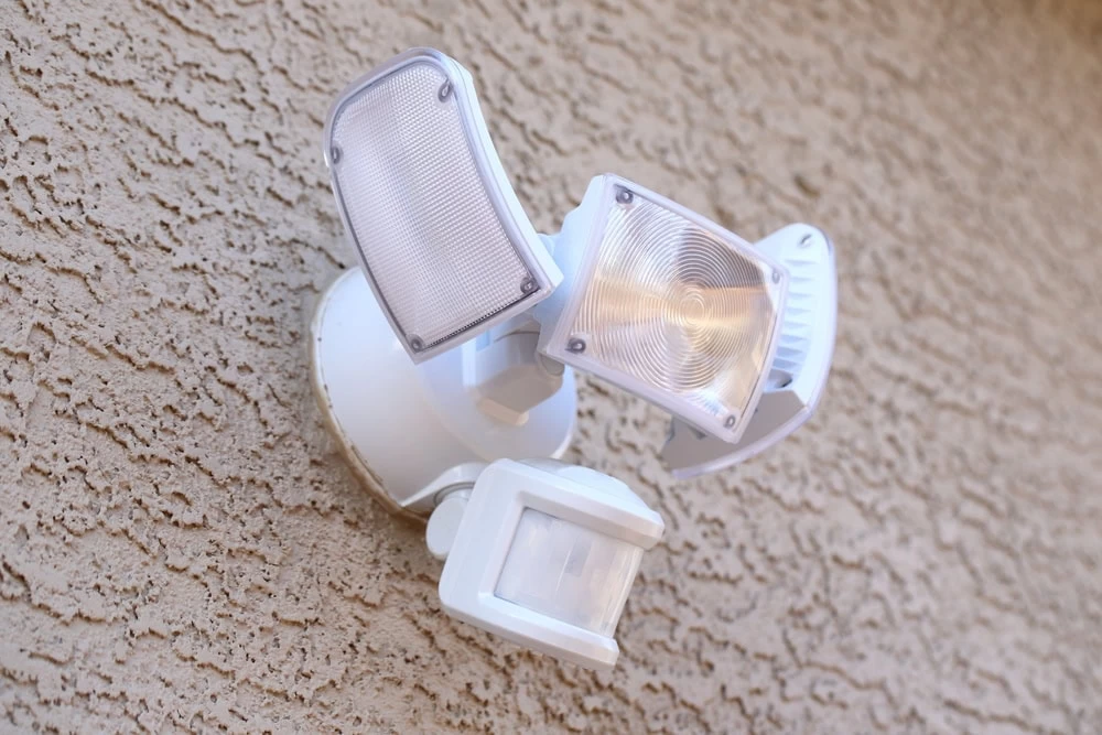 Motion Sensor Light - Taylor County, TX | Hooked Up Electric A security lighting solution features a motion sensor light with three adjustable panels, mounted on a textured beige wall. The two upper panels are sleek light fixtures, while the lower panel discreetly houses the motion sensor, enhancing both safety and style.